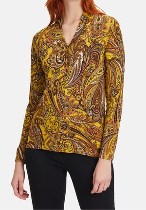 Blouse à manches longues en jaune avec un motif paisley complexe en marron, rouge et blanc. Dotée d'un col et d'une texture douce.