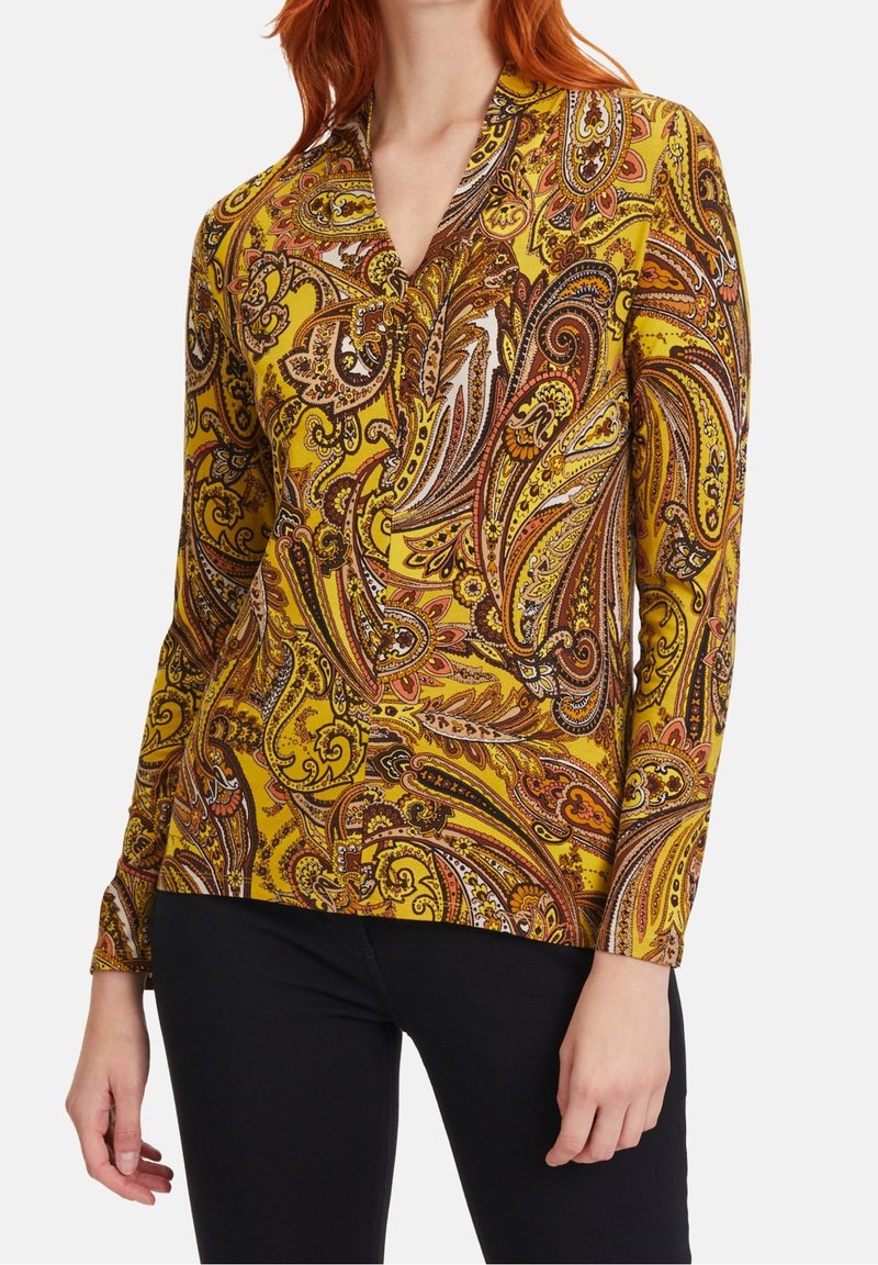 Blusa a maniche lunghe gialla con un intricato motivo paisley in marrone, rosso e bianco. Caratterizzata da un colletto e una texture morbida.
