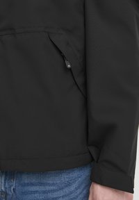 Črna lahka jakna z gladko teksturo tkanine, ki ima stranski žep na zadrgo in ravno spodnje rob.