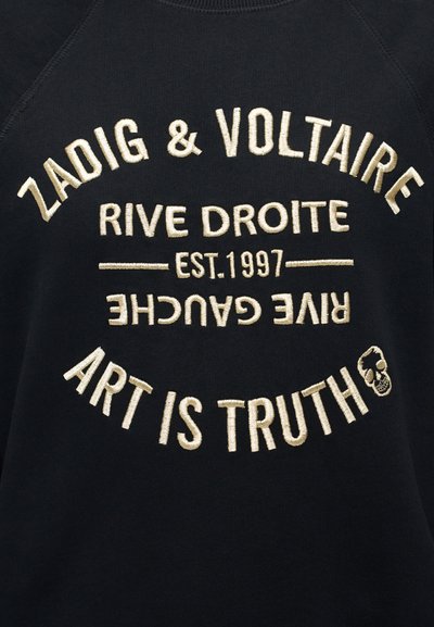 Μαύρο ύφασμα με μπεζ κεντημένο κείμενο: "ZADIG & VOLTAIRE," "RIVE DROITE," "EST. 1997," ανάποδα "RIVE GAUCHE," και "Η ΤΕΧΝΗ ΕΙΝΑΙ ΑΛΗΘΕΙΑ" με ένα μικρό κρανίο.