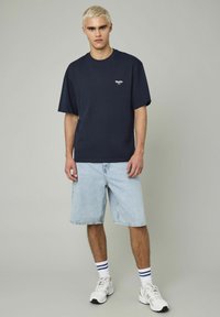 T-shirt en coton bleu marine à col rond et manches courtes, associé à un short en denim bleu clair. Le modèle porte des baskets blanches avec des chaussettes rayées.