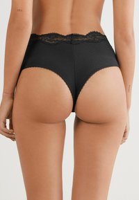 Culotte noire taille haute en tissu côtelé, avec une dentelle au niveau de la taille et un bord festonné le long des ouvertures de jambe.