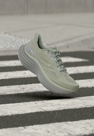 Chaussure de course vert clair avec une semelle épaisse en l'air au-dessus d'un passage piéton rayé noir et blanc.