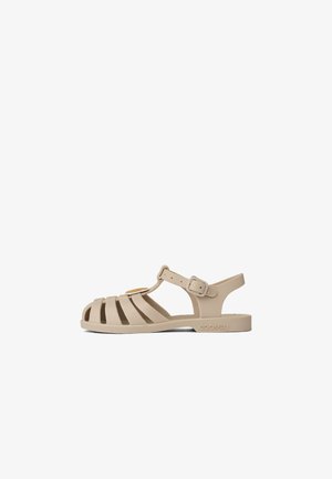 Beige rubber sandals with open toe, wide horizontal straps, adjustable ankle buckle, and logo detail on the sole. Flat sole design.