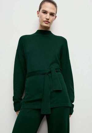 Suéter verde de manga larga con cuello alto y cintura ceñida, hecho de un tejido suave con un corte relajado y hombros caídos.