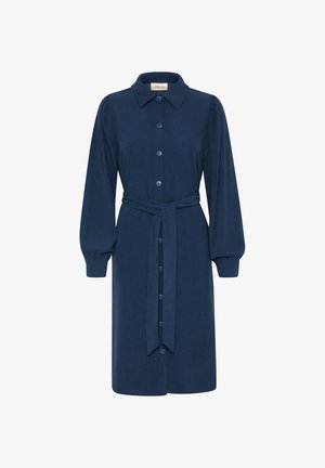 Tamno plava korduroj haljina s okovratnikom, prednjim dugmadi, dugim rukavima i pojasom. Karakterizira je nabrana ramena i rukavi s manžetama.