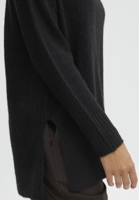 Czarny sweter z dzianiny z ribbowanym wzorem, długimi rękawami, bocznymi rozcięciami oraz luźnym krojem. Materiał wydaje się miękki i ciepły.