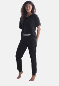 Musta puuvillainen vapaa-ajan vaatetussetti, joka sisältää rento-mallisen lyhythihaisen paidan ja kapenevat housut, joissa on joustava vyötärö ja brändätyt yksityiskohdat.