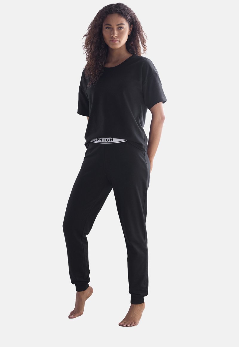 Musta puuvillainen vapaa-ajan vaatetussetti, joka sisältää rento-mallisen lyhythihaisen paidan ja kapenevat housut, joissa on joustava vyötärö ja brändätyt yksityiskohdat.