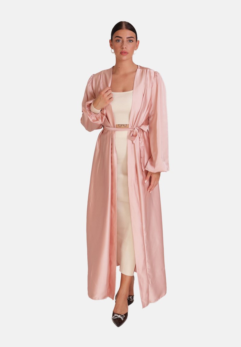 Lang pink satin morgenkåbe med brede ærmer, knyttet i taljen, lagd ovenpå en tætsiddende cremefarvet kjole. Fremhævet med skinnende sorte hæle.