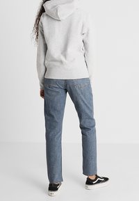 Gray hoodie with a drawstring hood, paired with blue jeans. Black sneakers with white soles. Texture appears soft, denim is sturdy.