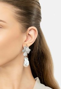Silver flower-shaped earrings with textured surface and a large, pear-shaped pearl drop. Features sparkling accents and intricate design details.