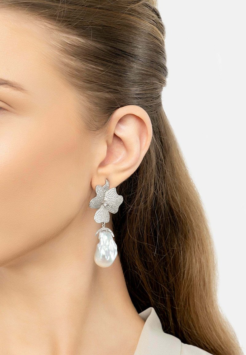 Silver flower-shaped earrings with textured surface and a large, pear-shaped pearl drop. Features sparkling accents and intricate design details.