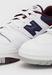 Baskets New Balance 550 blanches et bordeaux avec logo bleu marine et lacets blancs, montrant les détails côté et avant sur fond blanc.