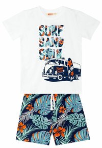 Valkoinen t-paita, jossa on sininen ja oranssi "SURF SAND SOUL" -teksti, ja jossa on vintage-vanin grafiikka. Yhdistettynä tummansinihin shortseihin, joissa on trooppinen lehtikuvio ja oransseja kukkia.