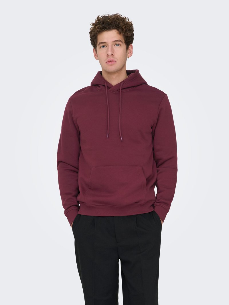 Burgundy hoodie made of soft fabric with a front pouch pocket, adjustable drawstring hood, and ribbed cuffs. Worn with black pants.