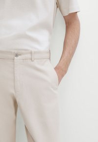 Beżowe bawełniane spodnie o slim fit, z zapięciem na guzik, kieszeniami bocznymi oraz gładką teksturą. W komplecie z jasnobeżową koszulą.
