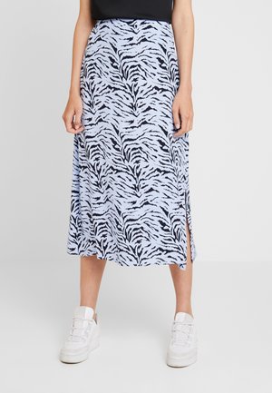 Kobieta ubrana w jasnoniebieską midi spódnicę w czarny wzór zebry z rozcięciem po boku, białe trampki i czarną bluzkę, sfotografowana od talii w dół.
