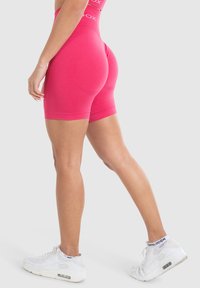 Fuchsia gestreepte shorts met een hoge tailleband en een gladde textuur, gecombineerd met witte sportsneakers. Accenten met logodetails.