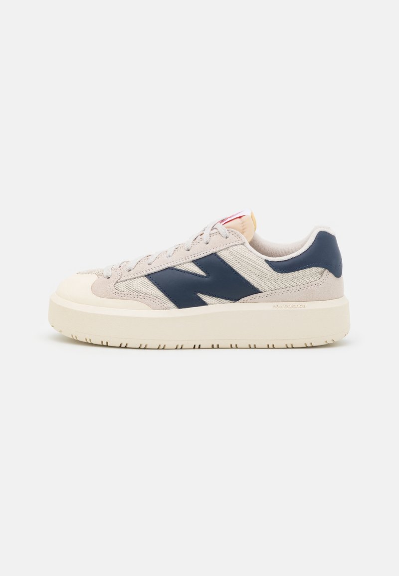 Beige lave sneakers med navyblåt sidelogo, hvid tyk sål og beige snørebånd på hvid baggrund.