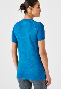 Camiseta deportiva de manga corta azul, hecha de tejido texturizado, con un patrón geométrico en la parte posterior y costuras de acento a lo largo de los hombros.