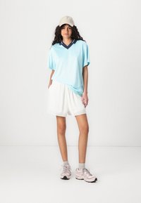 Helesinine V-keljega särk tumesinise kraega, mille juurde on kombineeritud valged tekstuuriga lühikesed püksid, millel on pitsääris. Kanda hallide sokkide ja roosade sportjalatsitega.