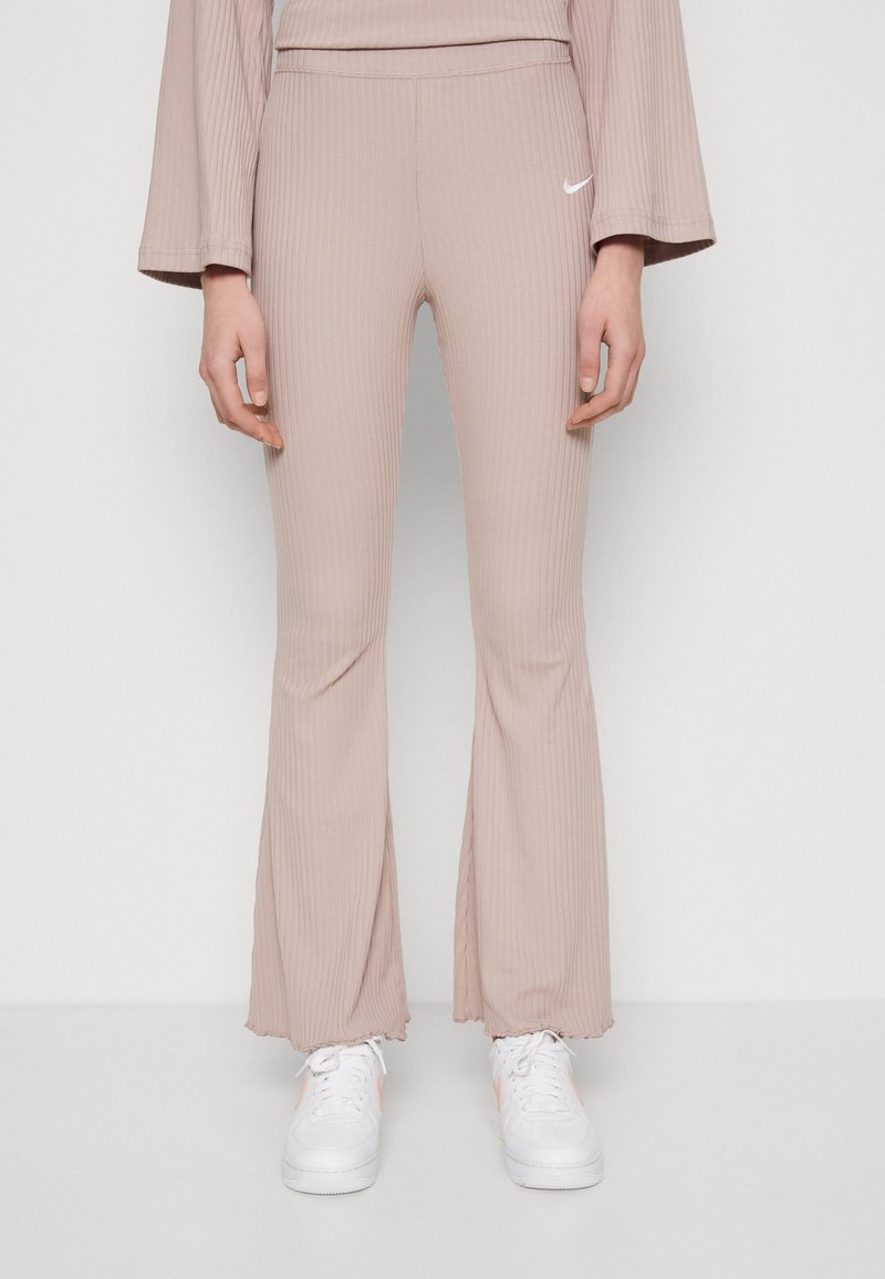 Ljust rosa ribbade utsvängda byxor med en mjuk textur och Nike-logga på midjan, tillsammans med vita sneakers med en subtil accent.