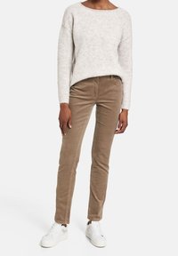 Pantalons en velours côtelé beige avec une coupe slim, présentant une taille mi-haute et des côtes verticales subtiles, associés à un pull en mailles gris clair et des baskets blanches.