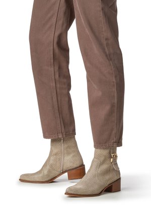 Beige enkellaarsjes in slangenprint met een zijrits, langwerpige punten en een gestapelde bruine hak, gecombineerd met bruine taps toelopende broek.