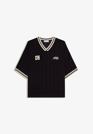 Pull en maille noir à manches courtes avec col en V blanc et rayures sur les manches, numéro « 09 » sur la poitrine gauche et inscription « Good Supply » sur la poitrine droite.
