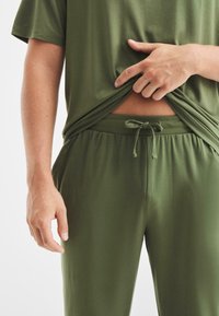 Camicia verde oliva a maniche corte realizzata in tessuto morbido con una vestibilità comoda, abbinata a pantaloni con coulisse in tinta unita e vita elastica.