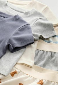 Assorted children's clothing, including a blue T-shirt, gray T-shirt, cream shirt, and patterned shorts featuring teddy bears, showcasing soft cotton fabric.