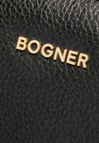 Pelle nera testurizzata con un prominente logo dorato "BOGNER" in lettere maiuscole. La superficie è irregolare con una finitura a grana.