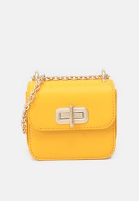 Żółta skórzana torebka o prostokątnym kształcie, z przednią klapą i metalowym zapięciem. Posiada złotą łańcuszkową rączkę oraz szczegóły przeszycia.