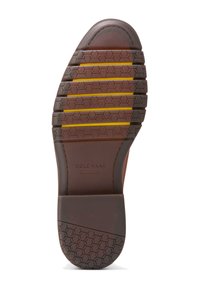 Hnědá gumová podrážka s hexagonálním vzorem pro trakci. Obsahuje žluté akcenty v drážkách. Označeno "COLE HAAN", s flexibilními drážkami na patě.