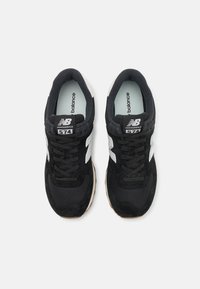 Black New Balance 574 sneakers feature a suede and mesh upper, white logo accents, and a gum rubber sole. Classic lace-up design.