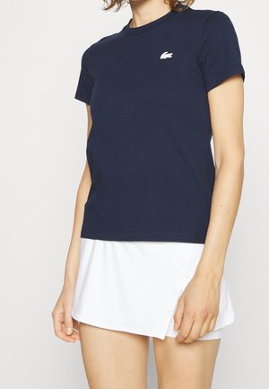 T-shirt en coton marine à manches courtes et col ras du cou. Présente un logo blanc sur la poitrine. Associé à une jupe blanche évasée.