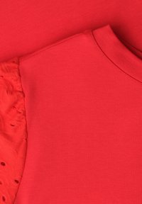 Tissu rouge montrant un gros plan d’un vêtement avec un corps uni et une manche bouffante texturée à motif œillet.