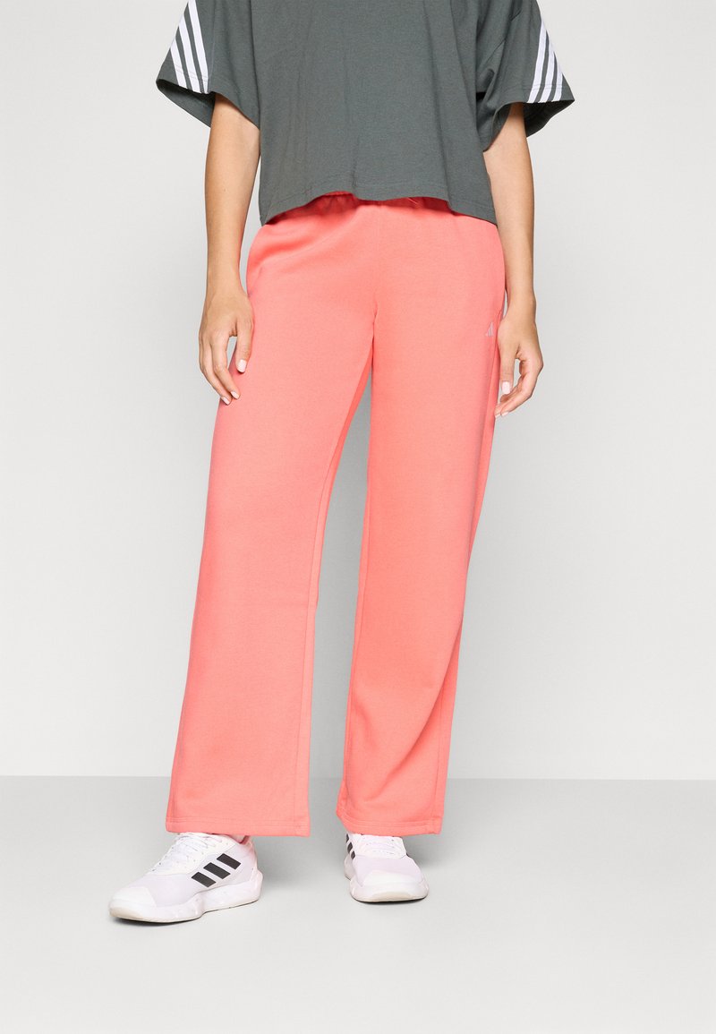 Coral sweatpants with a relaxed fit, elastic waistband, and side pockets. Paired with a grey t-shirt and white athletic shoes.