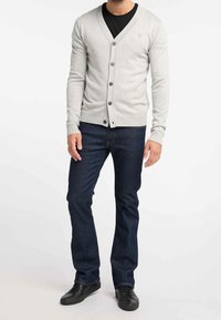 Cardigan grigio chiaro con scollo a V, chiusura con bottoni e polsini a coste, indossato sopra una camicia nera. Abbinato a jeans blu scuro e scarpe nere.