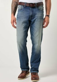 Jeans de mezclilla azul claro con corte recto, sutil desgaste y diseño de cinco bolsillos. Combinados con botas y cinturón de cuero marrón.