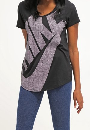 T-shirt nero a maniche corte con un grande logo Nike bianco verticale, caratterizzato da una texture a righe e un orlo arrotondato. Indossato con jeans blu.