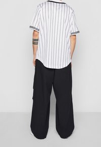 Camicetta bianca a maniche corte con strisce verticali nere, orlo arrotondato, abbinata a pantaloni neri larghi e morbidi.
