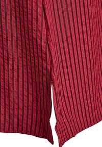 Červená pruhovaná látka s kontrastnými tmavými pruhmi, s dizajnom s rozparkom. Textúra vyzerá jemne a materiál pôsobí hladko.