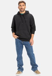 Black hoodie with a front pocket and drawstrings, paired with blue denim jeans and beige shoes. Plain design with no visible patterns.