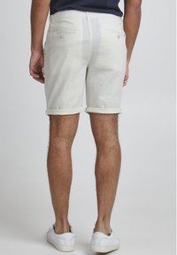 Pantalones cortos de lino blancos con dobladillo enrollado, que cuentan con dos bolsillos traseros y costuras en contraste. Llevados con zapatillas blancas.