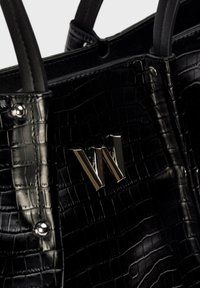 Czarna torba tote w wzór krokodylej skóry z metalowymi akcentami i gładkimi uchwytami. Torba zawiera złoty detal z logo "W" wyraźnie widoczny.