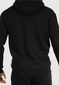 Felpa nera con cappuccio in stile kangaroo, polsini e orlo a costine, e cappuccio foderato. Realizzata in un morbido tessuto testurizzato.