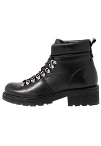 Zwarte leren enkelboot met dikke zool, metalen oogjes, zwart-rode veters, gevoerde kraag en lage blokhak tegen een witte achtergrond.