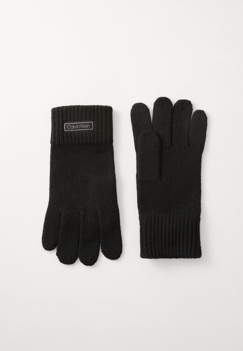 Black knit gloves with a ribbed cuff, featuring a rectangular Calvin Klein label on the wrist area. Five-finger design, soft texture.